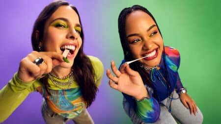 Trident no Rock in Rio 2026 com “Que se Masque” Duas mulheres sorrindo e fazendo pose com um objeto verde e branco na boca, em clima de evento ao fundo roxo e azul.